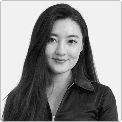 About Us: Woman with long hair wearing a zip-up collared shirt, looking at the camera and smiling softly against a plain background.