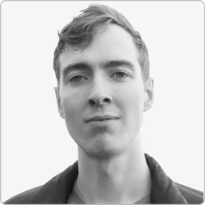 A young man with short hair looks directly at the camera with a neutral expression, wearing a jacket, on a light background—an image that reflects the approachable and professional spirit of our About Us page.