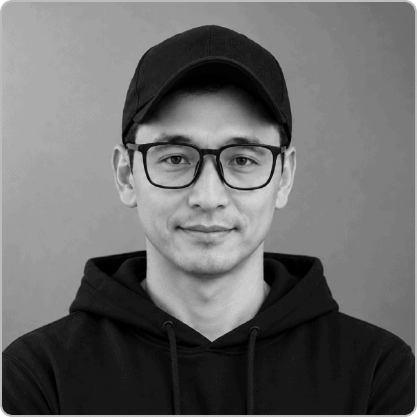A man wearing glasses, a black cap, and a black hoodie looks at the camera with a neutral expression against a plain background, embodying the approachable and authentic spirit of our About Us page.
